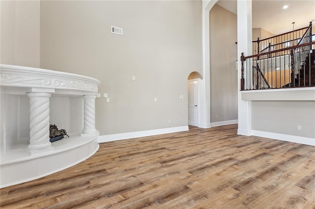 unfurnished living room with arched walkways, visible vents, baseboards, and wood finished floors