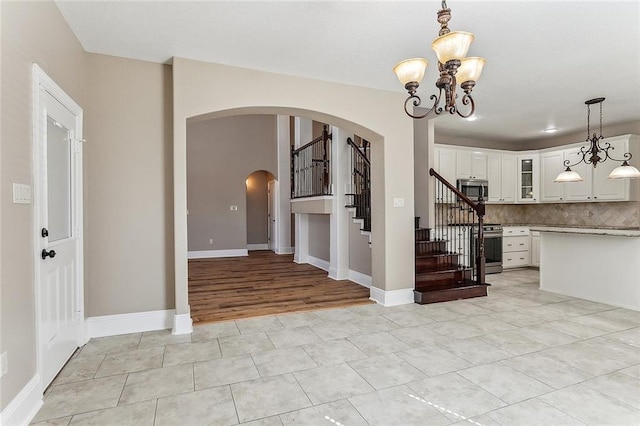 entryway with light tile patterned floors, baseboards, arched walkways, stairway, and a notable chandelier