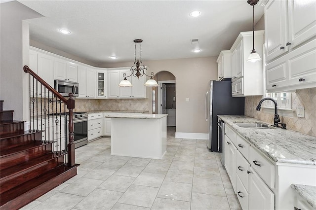 kitchen with arched walkways, stainless steel appliances, a kitchen island, a sink, and visible vents