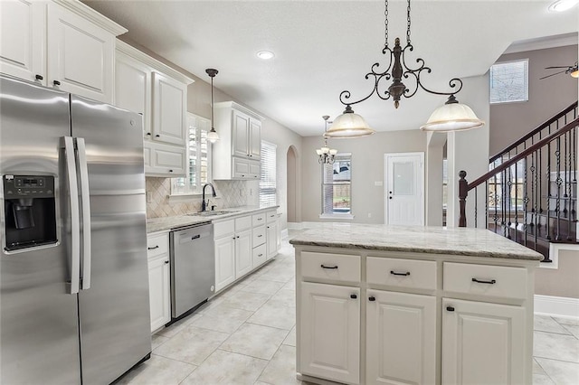 kitchen featuring arched walkways, stainless steel appliances, a sink, white cabinets, and backsplash