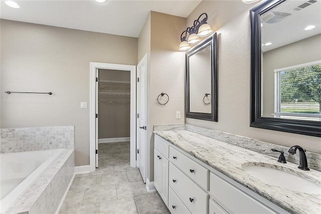 full bath with double vanity, tile patterned floors, a garden tub, a walk in closet, and a sink