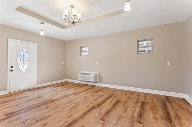 entryway featuring light wood-style floors, a wall mounted air conditioner, a raised ceiling, and baseboards