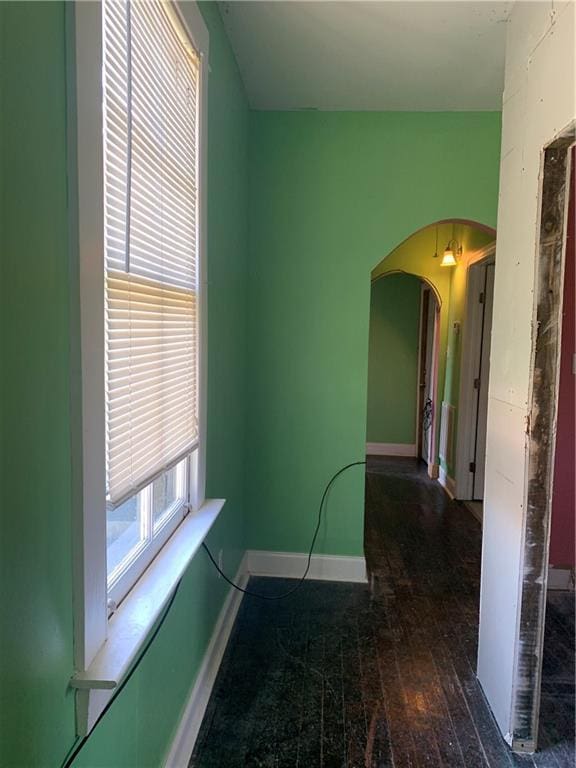 empty room with arched walkways, wood-type flooring, and baseboards