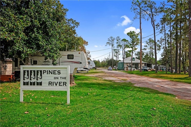 community sign featuring dirt driveway and a yard