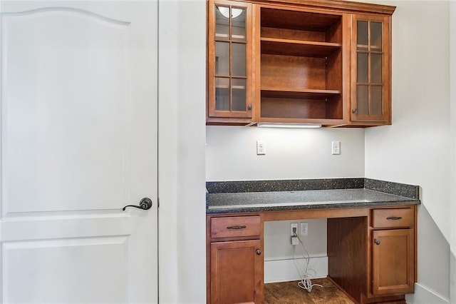 interior space featuring brown cabinets, open shelves, glass insert cabinets, built in study area, and dark stone counters