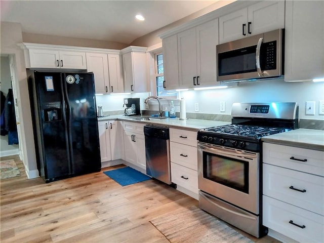 kitchen with light wood finished floors, stainless steel appliances, light countertops, white cabinets, and a sink