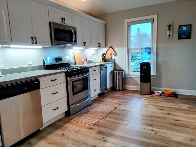 kitchen featuring light wood finished floors, appliances with stainless steel finishes, white cabinets, and baseboards