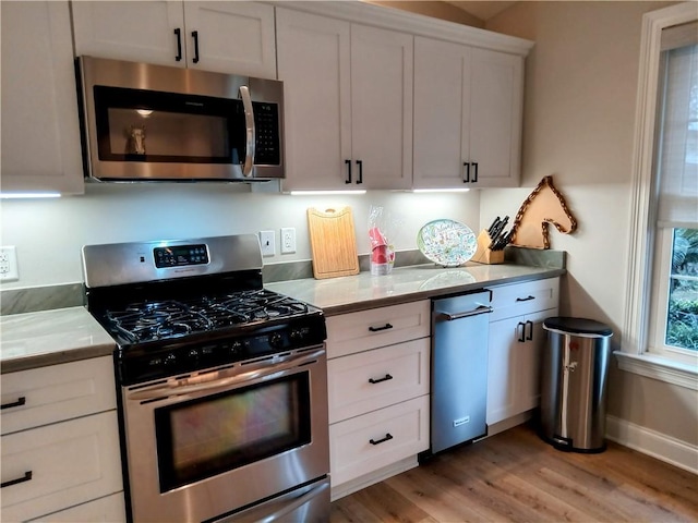 kitchen with appliances with stainless steel finishes, light wood-style flooring, white cabinetry, and baseboards