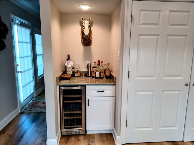 bar with a dry bar, beverage cooler, baseboards, and light wood-style flooring