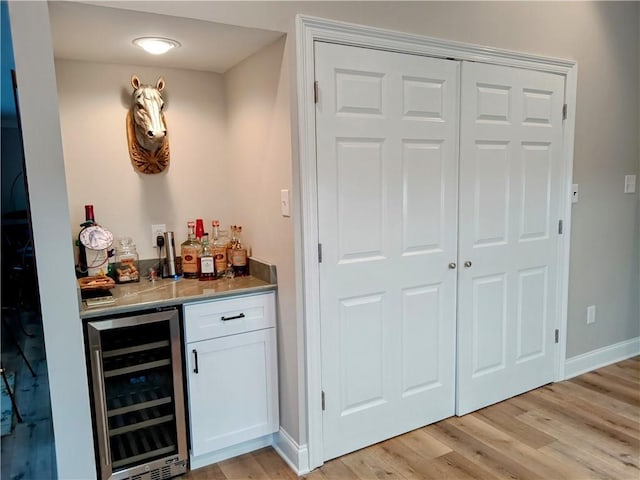 bar with light wood-type flooring, wine cooler, baseboards, and a dry bar