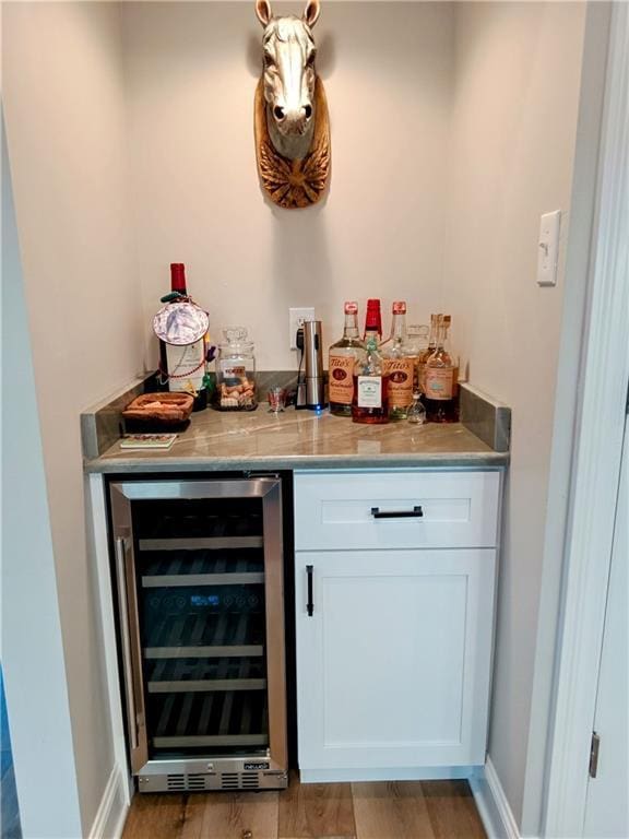 bar featuring a bar, wine cooler, light wood-type flooring, and baseboards