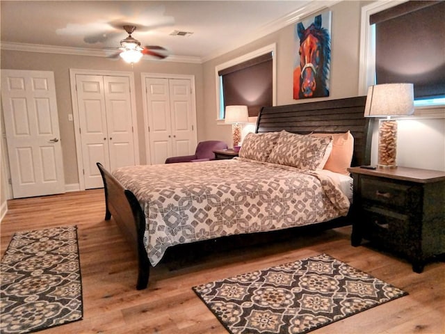 bedroom featuring visible vents, ceiling fan, wood finished floors, crown molding, and multiple closets