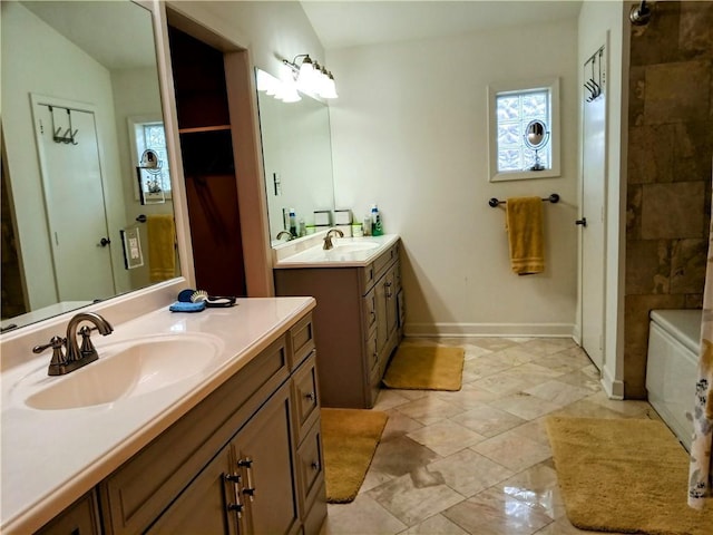 bathroom with a tub, baseboards, two vanities, and a sink