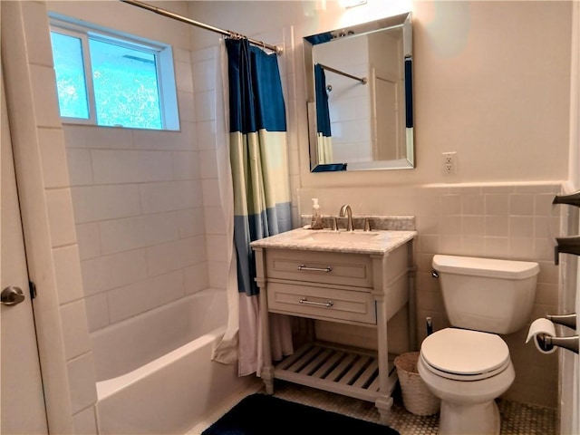 bathroom featuring toilet, a wainscoted wall, shower / bath combination with curtain, vanity, and tile walls