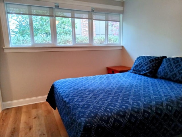 bedroom with multiple windows, baseboards, and wood finished floors