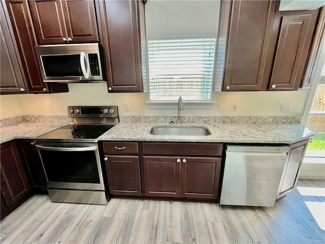 kitchen with appliances with stainless steel finishes, a sink, light wood-style flooring, and dark brown cabinetry