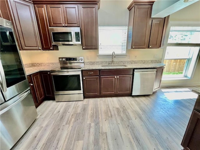 kitchen featuring light wood finished floors, appliances with stainless steel finishes, dark brown cabinetry, a sink, and light stone countertops