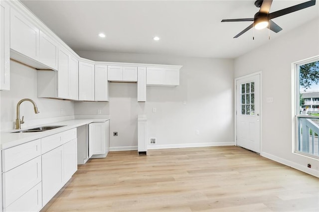 kitchen featuring recessed lighting, a sink, white cabinetry, baseboards, and light wood-type flooring