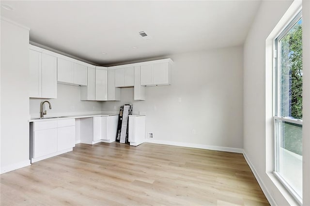 kitchen featuring visible vents, light wood-style flooring, light countertops, white cabinetry, and a sink