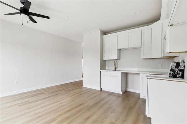 kitchen featuring ceiling fan, light wood-style flooring, a sink, white cabinets, and baseboards