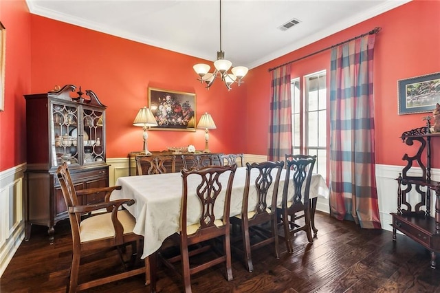 dining space with a chandelier, wood finished floors, visible vents, ornamental molding, and wainscoting