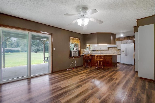 kitchen with a breakfast bar area, a peninsula, white refrigerator with ice dispenser, dark wood-type flooring, and decorative backsplash