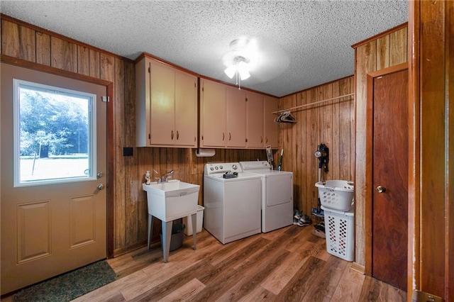 laundry area with light wood-style floors, washing machine and clothes dryer, cabinet space, and wooden walls