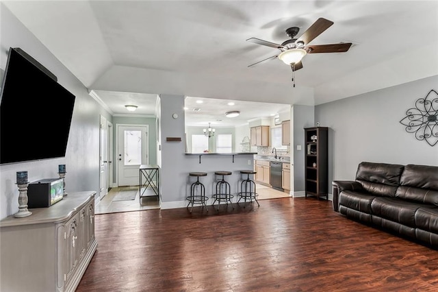 living room featuring crown molding, lofted ceiling, light wood-type flooring, baseboards, and ceiling fan with notable chandelier