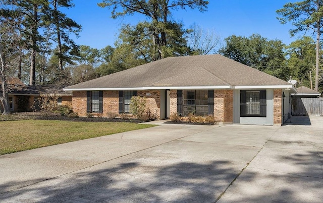 single story home with concrete driveway, brick siding, roof with shingles, and a front yard