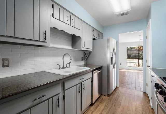 kitchen featuring gas range oven, dark countertops, visible vents, stainless steel dishwasher, and a sink