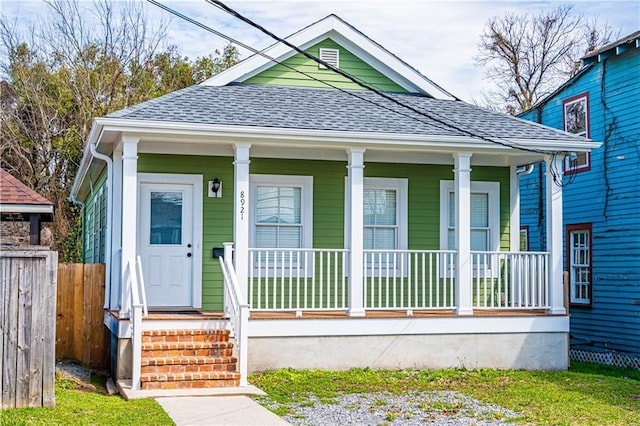 view of front of house with covered porch, roof with shingles, and fence