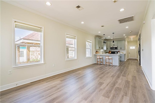 kitchen featuring ornamental molding, stainless steel microwave, a kitchen bar, and visible vents