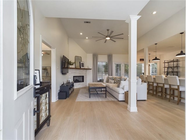 living area with light wood-style floors, a fireplace, a ceiling fan, and ornate columns