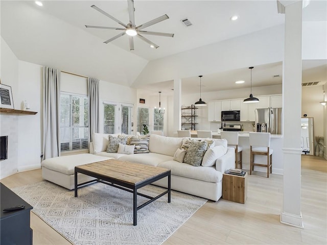 living area with light wood finished floors, lofted ceiling, visible vents, a tiled fireplace, and ceiling fan