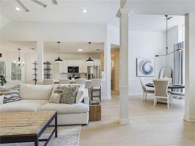 living room with light wood-type flooring, ornate columns, an inviting chandelier, and recessed lighting