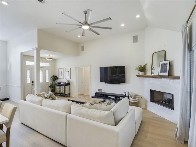 living area with recessed lighting, a ceiling fan, light wood-type flooring, a glass covered fireplace, and decorative columns