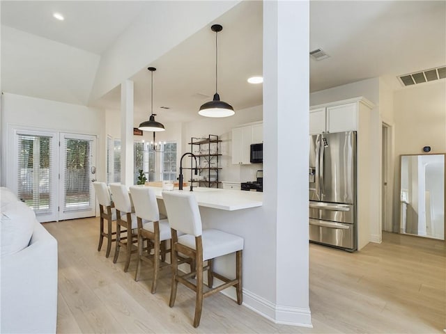 kitchen featuring black microwave, a breakfast bar area, stove, visible vents, and stainless steel fridge