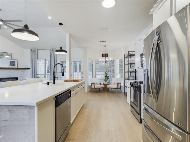 kitchen featuring open floor plan, stainless steel appliances, light countertops, a fireplace, and ceiling fan with notable chandelier