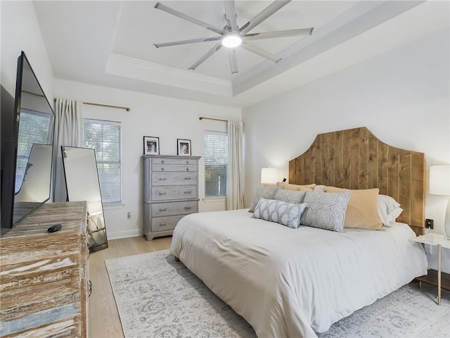 bedroom with a ceiling fan, baseboards, light wood-style floors, a raised ceiling, and crown molding