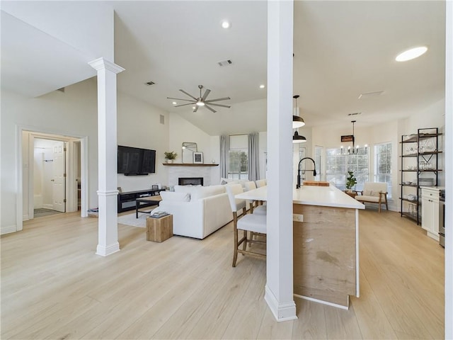 living room with lofted ceiling, decorative columns, and light wood-style flooring