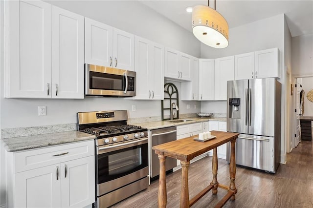 kitchen with light stone counters, white cabinets, stainless steel appliances, and wood finished floors