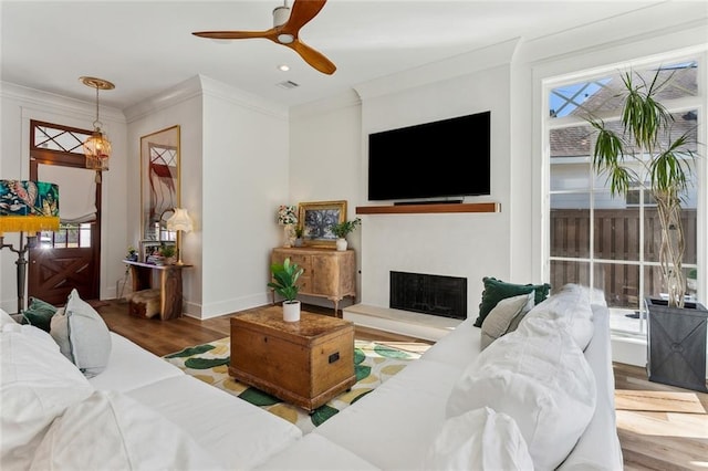 living area with baseboards, visible vents, a fireplace with raised hearth, ornamental molding, and wood finished floors