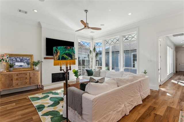 living room with ornamental molding, visible vents, a fireplace with raised hearth, and wood finished floors