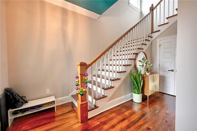 staircase with crown molding, a high ceiling, wood finished floors, and baseboards