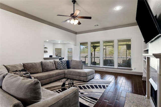 living area with arched walkways, crown molding, a fireplace, wood finished floors, and baseboards