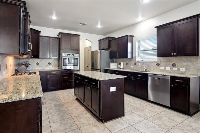 kitchen with arched walkways, a center island, stainless steel appliances, visible vents, and a sink