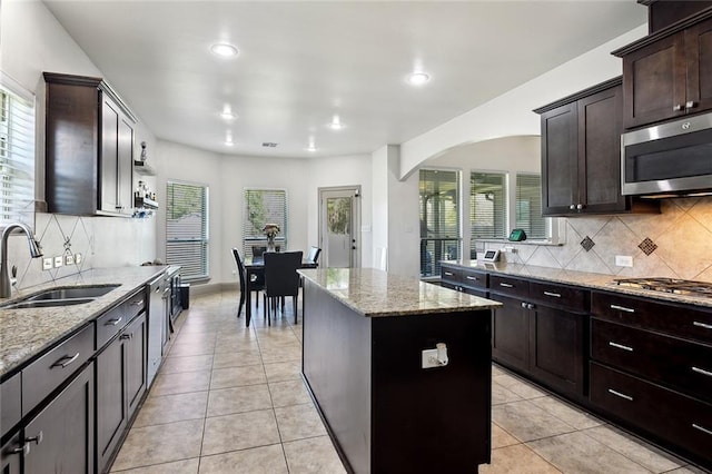 kitchen with light tile patterned floors, arched walkways, a kitchen island, stainless steel appliances, and a sink