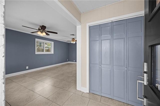 unfurnished bedroom with light tile patterned floors, baseboards, a ceiling fan, crown molding, and a closet