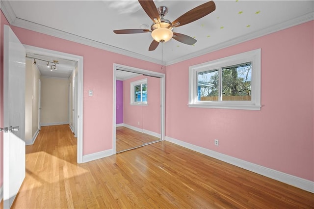 unfurnished bedroom featuring crown molding, a closet, light wood-style flooring, a ceiling fan, and baseboards