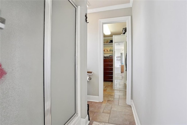 hallway with crown molding, baseboards, and stone tile flooring